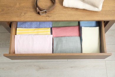 Chest of drawers with different folded clothes and belt indoors, top view