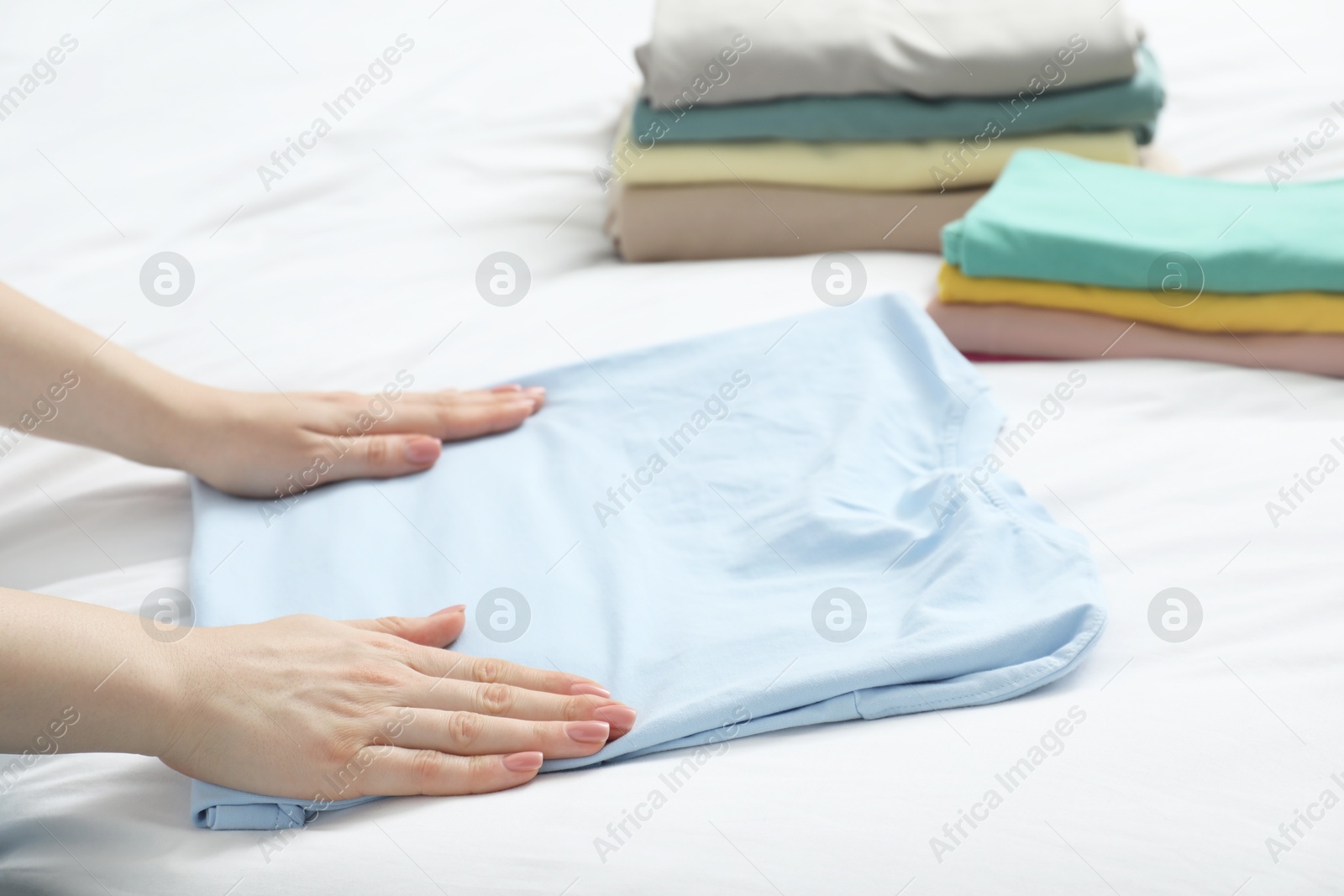 Photo of Woman folding clothes on bed, closeup view