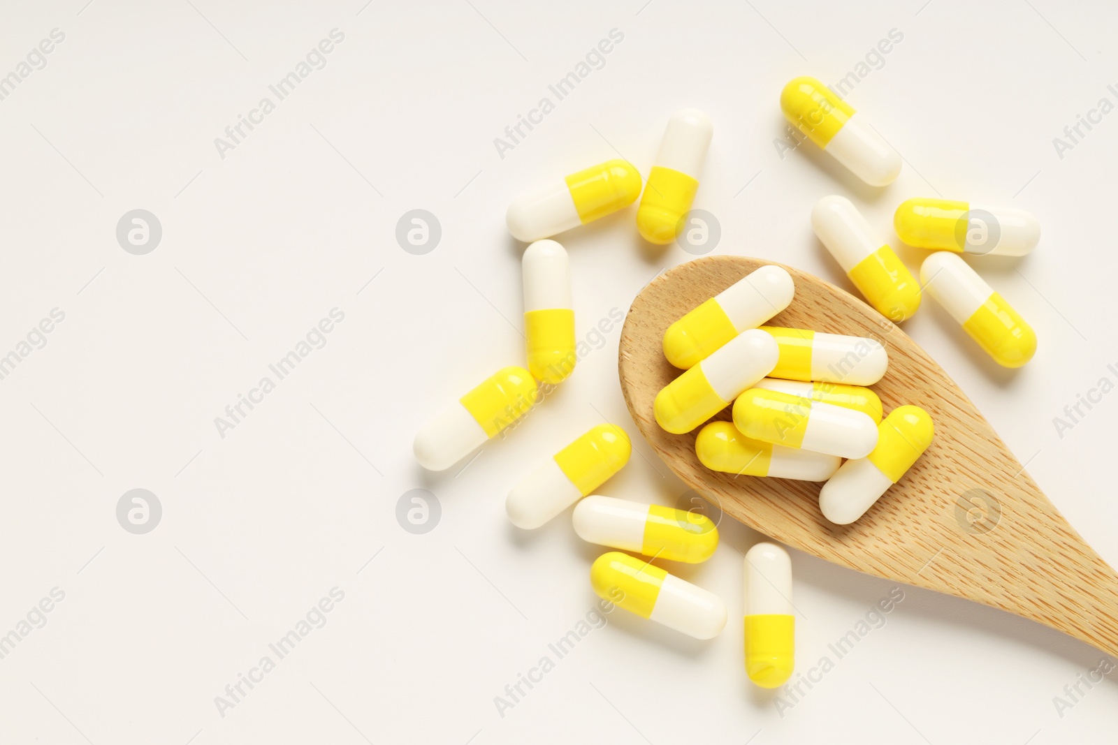 Photo of Antibiotic pills and spoon on white background, top view. Space for text