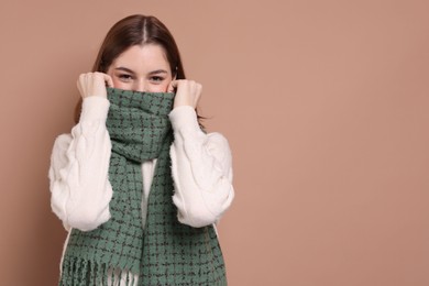 Beautiful woman in warm scarf on brown background, space for text