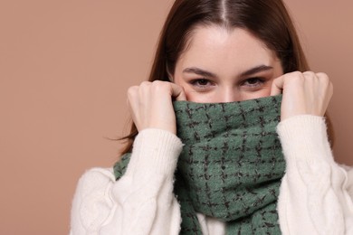 Beautiful woman in warm scarf on brown background, space for text