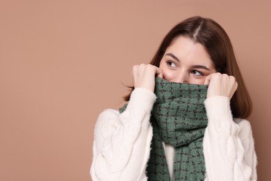 Beautiful woman in warm scarf on brown background, space for text