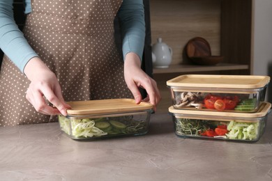 Healthy food. Woman closing glass containers with fresh vegetables at grey table, closeup