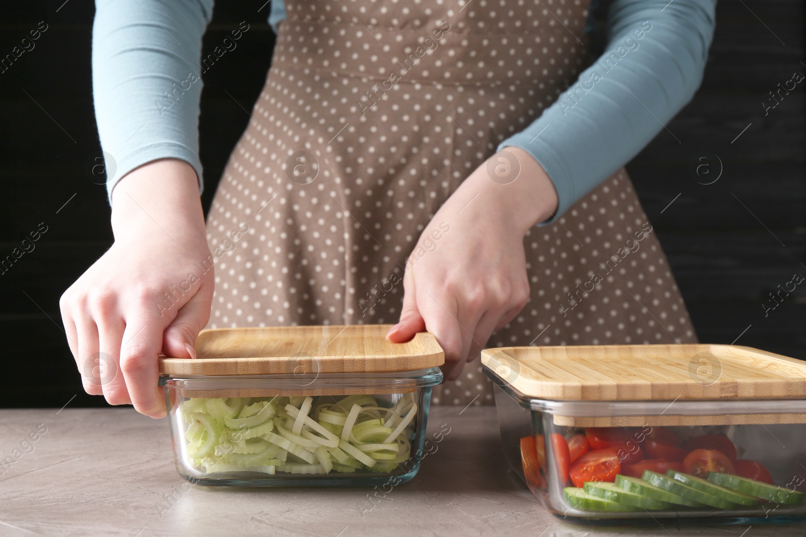 Photo of Healthy food. Woman closing glass containers with fresh vegetables at grey table, closeup