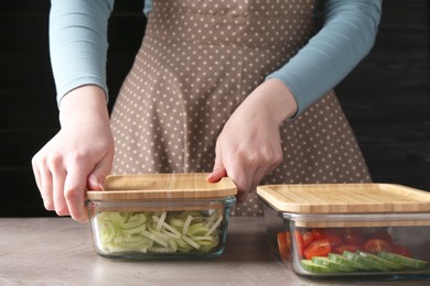 Healthy food. Woman closing glass containers with fresh vegetables at grey table, closeup