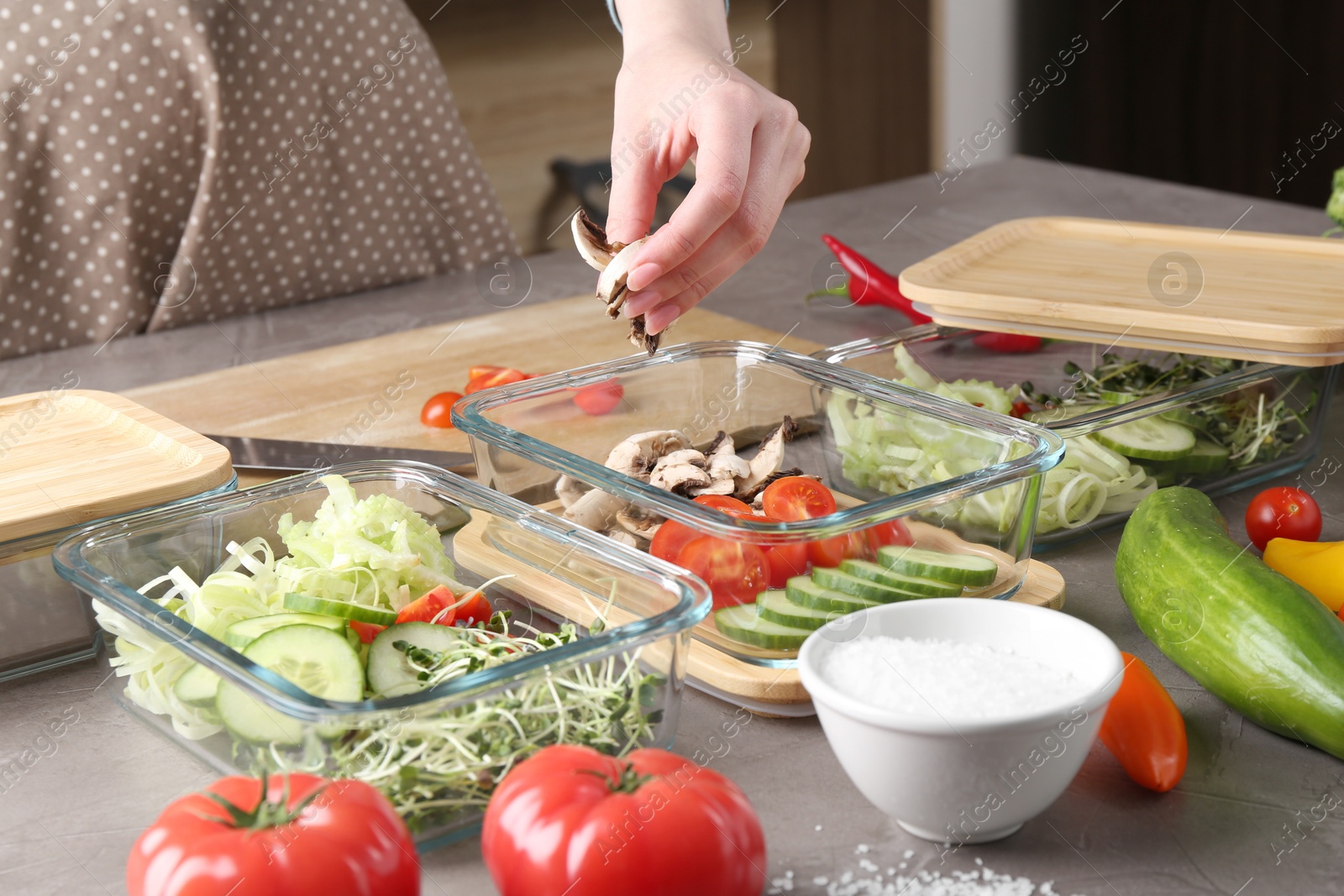 Photo of Healthy food. Woman putting pieces of champignons into glass container at grey table in kitchen, closeup