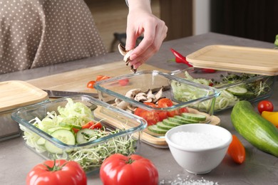 Healthy food. Woman putting pieces of champignons into glass container at grey table in kitchen, closeup