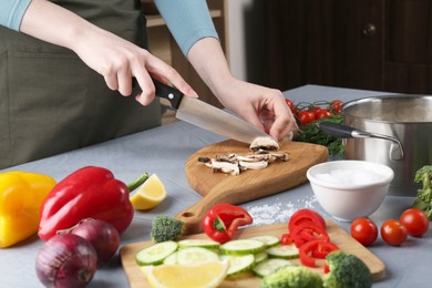 Photo of Healthy food. Woman cutting champignon at grey table, closeup