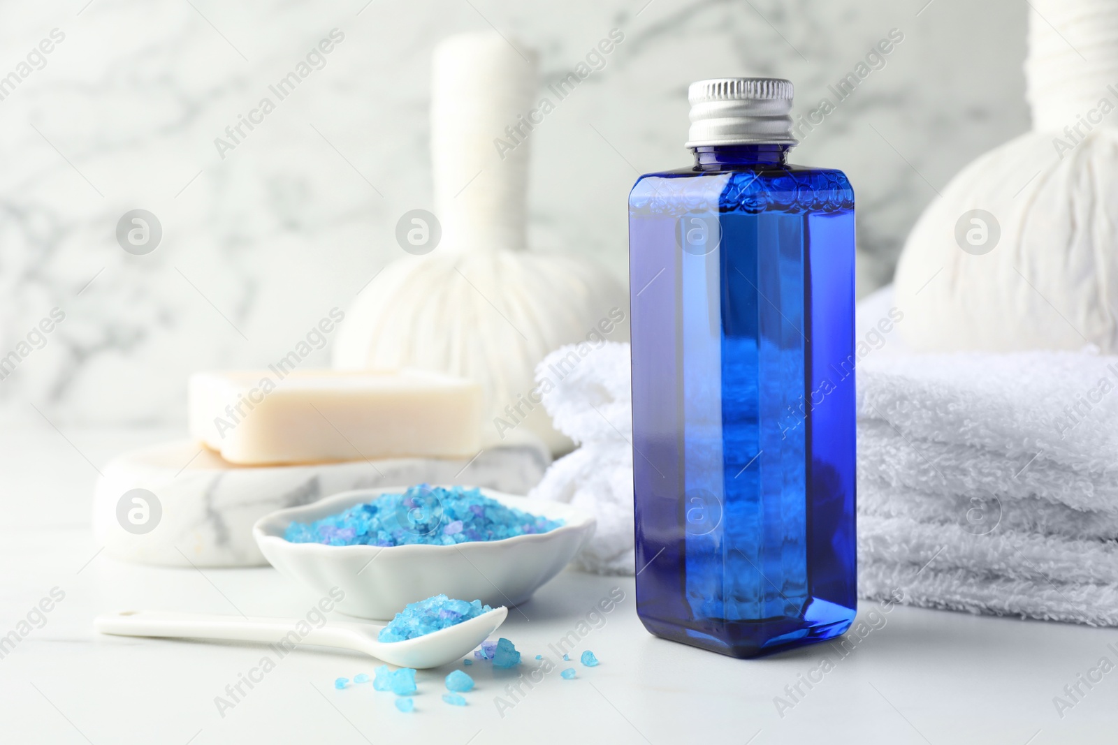 Photo of Spa composition. Bottle of cosmetic product, sea salt, towel, soap and herbal bags on white table