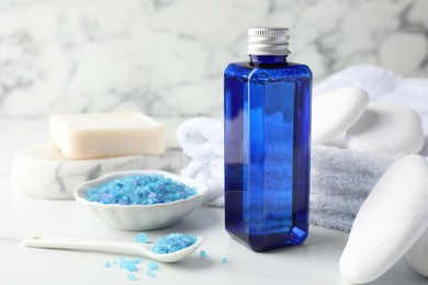 Photo of Spa composition. Bottle of cosmetic product, sea salt, towel, stones and soap on white table