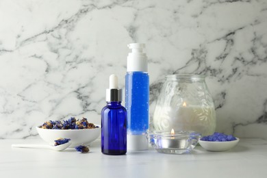 Spa composition. Bottles of cosmetic products, dry flowers and burning candles on white marble table