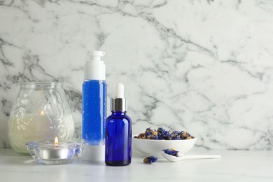 Photo of Spa composition. Bottles of cosmetic products, dry flowers and burning candles on white marble table, space for text