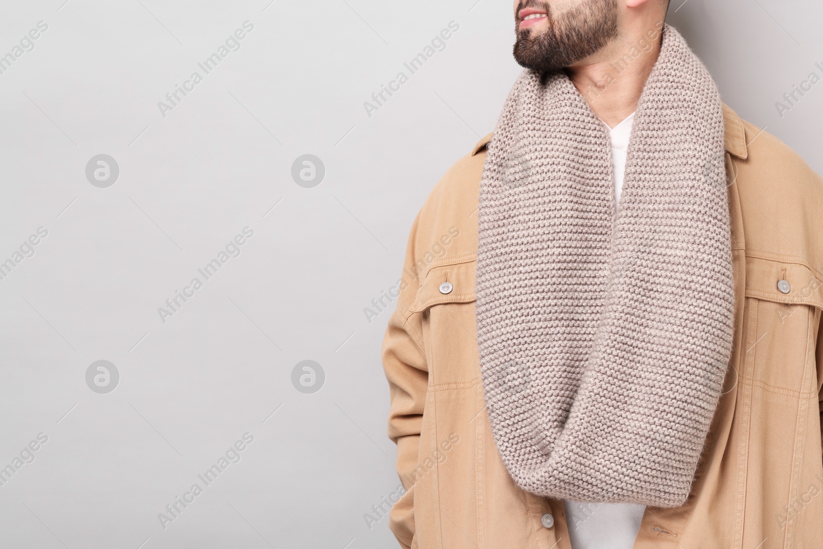 Photo of Smiling man in warm scarf on light grey background, closeup. Space for text