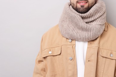 Smiling man in warm scarf on light grey background, closeup. Space for text