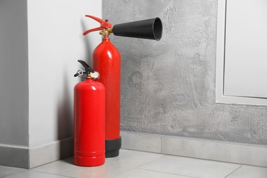 Photo of Fire extinguishers on floor near grey wall indoors