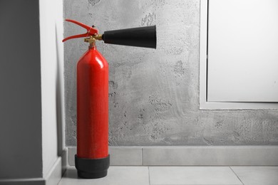 Photo of Fire extinguisher on floor near grey wall indoors, space for text