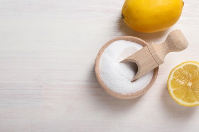 Photo of Baking soda and lemons on white wooden table, top view. Space for text