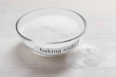 Photo of Baking soda in bowl on white wooden table, closeup