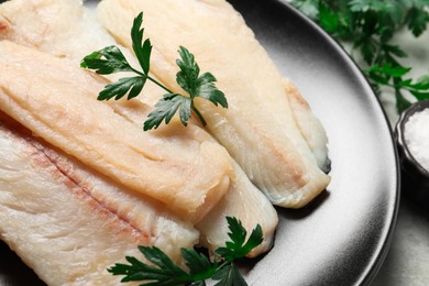 Plate with raw cod fish and parsley on table, closeup