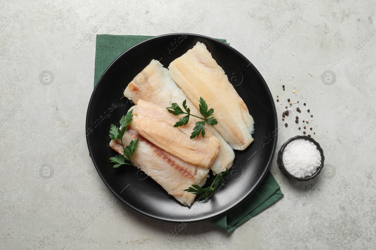 Photo of Plate with raw cod fish, spices and parsley on light table, flat lay