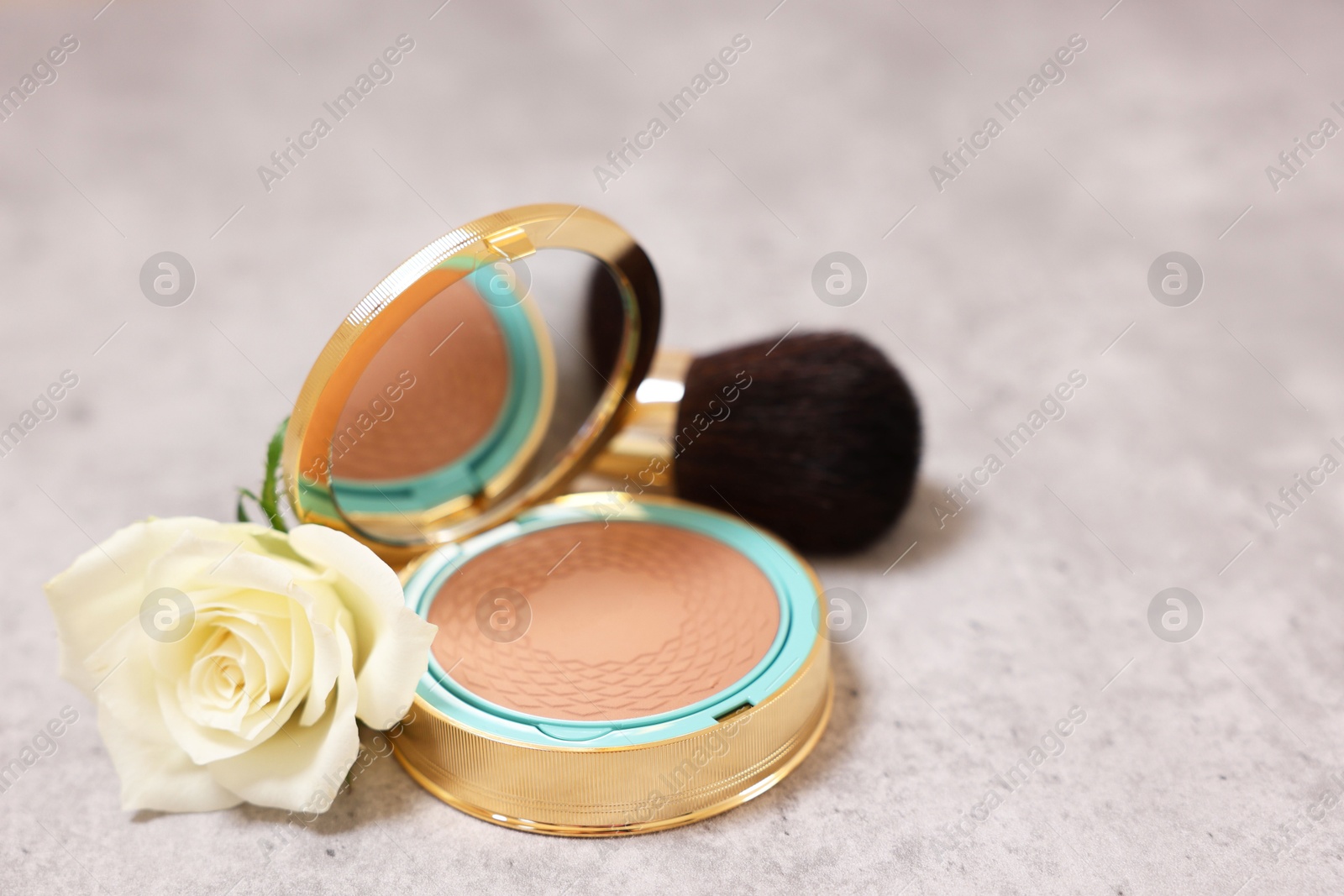 Photo of Bronzer, brush and rose flower on grey textured table, closeup. Space for text