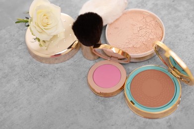 Bronzer, powder, blusher, brush and rose flower on grey textured table, above view
