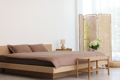 Photo of Folding screen, comfortable bed, ottoman and bedside table in room