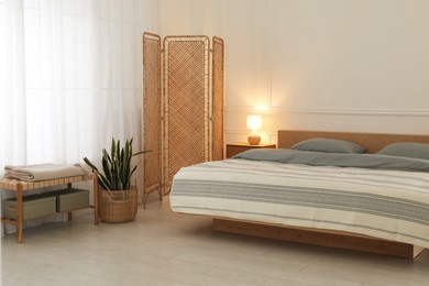 Stylish bedroom with double bed and beautiful green houseplant. Modern interior