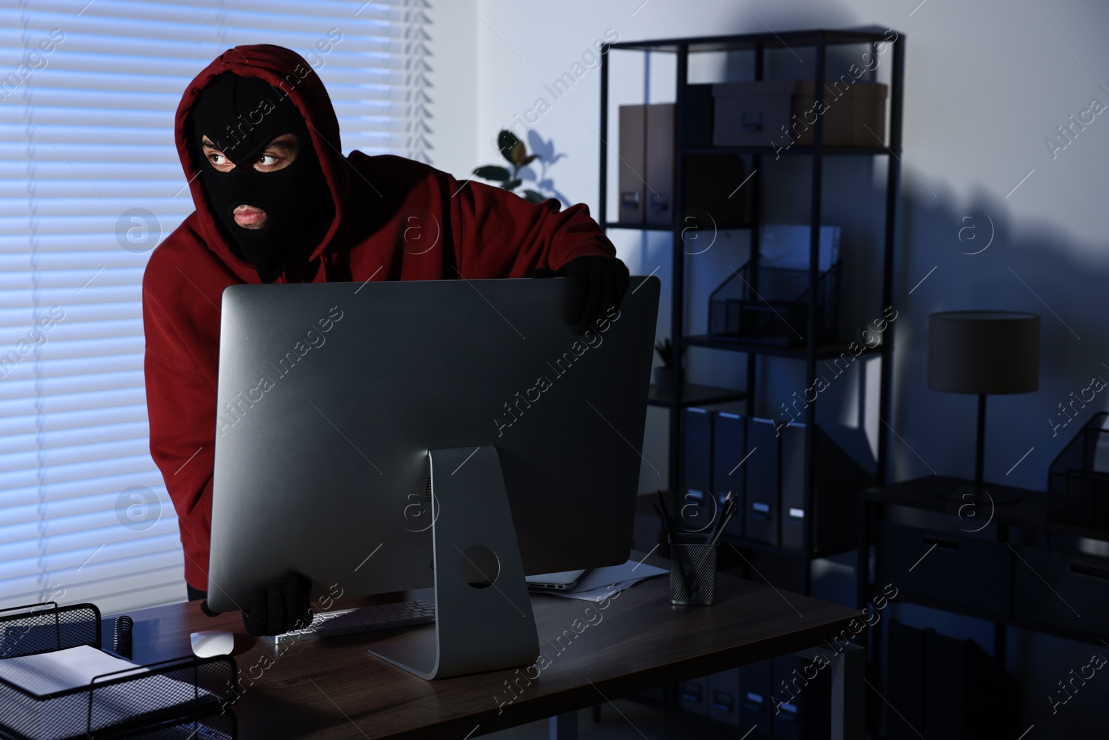 Photo of Thief stealing computer monitor in office at night. Burglary