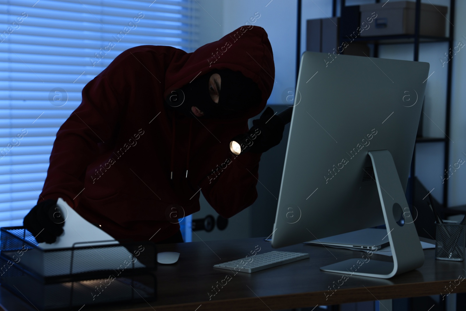 Photo of Thief with flashlight looking for money in office at night. Burglary