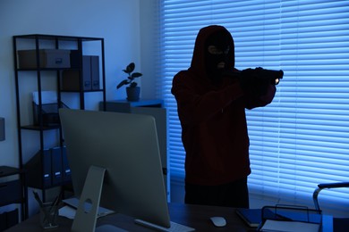 Thief with flashlight and gun in office at night. Burglary