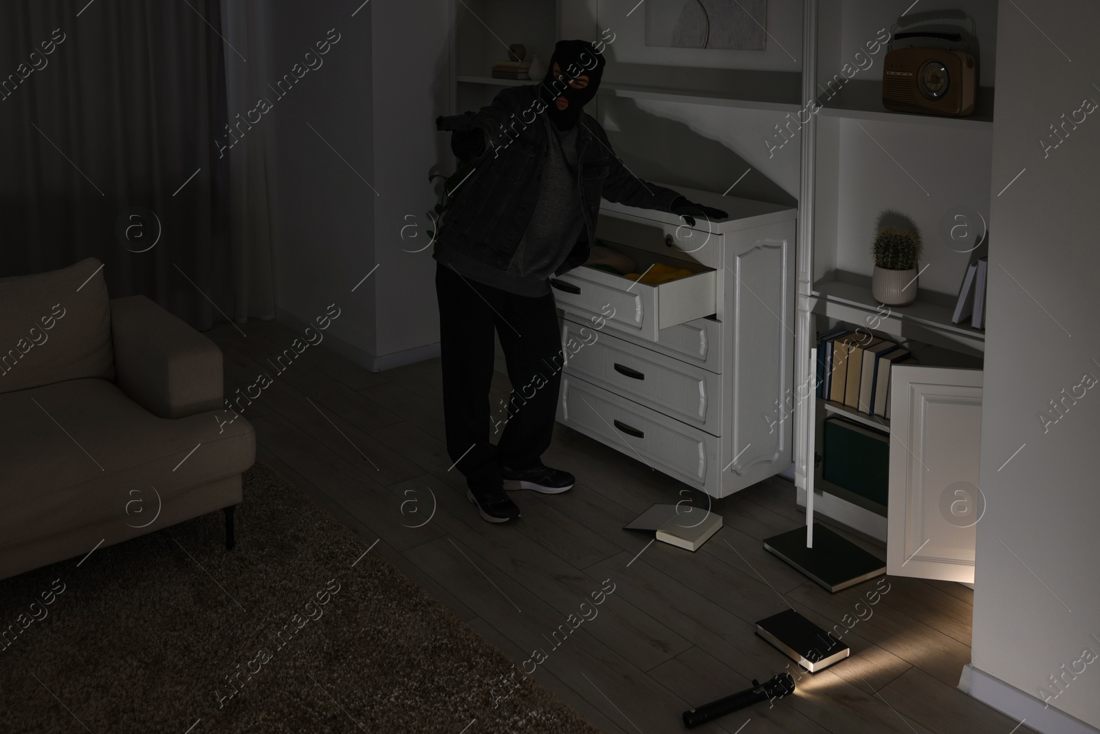 Photo of Thief with gun near chest of drawers at foreign house. Burglary