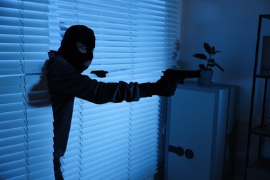 Thief with gun coming out of blinds at night. Burglary