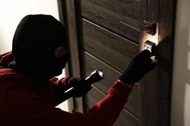 Thief with flashlight breaking foreign door's lock in hall. Burglary