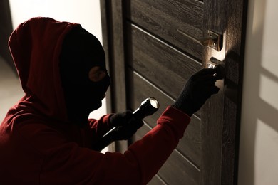 Photo of Thief with flashlight breaking foreign door's lock in hall. Burglary