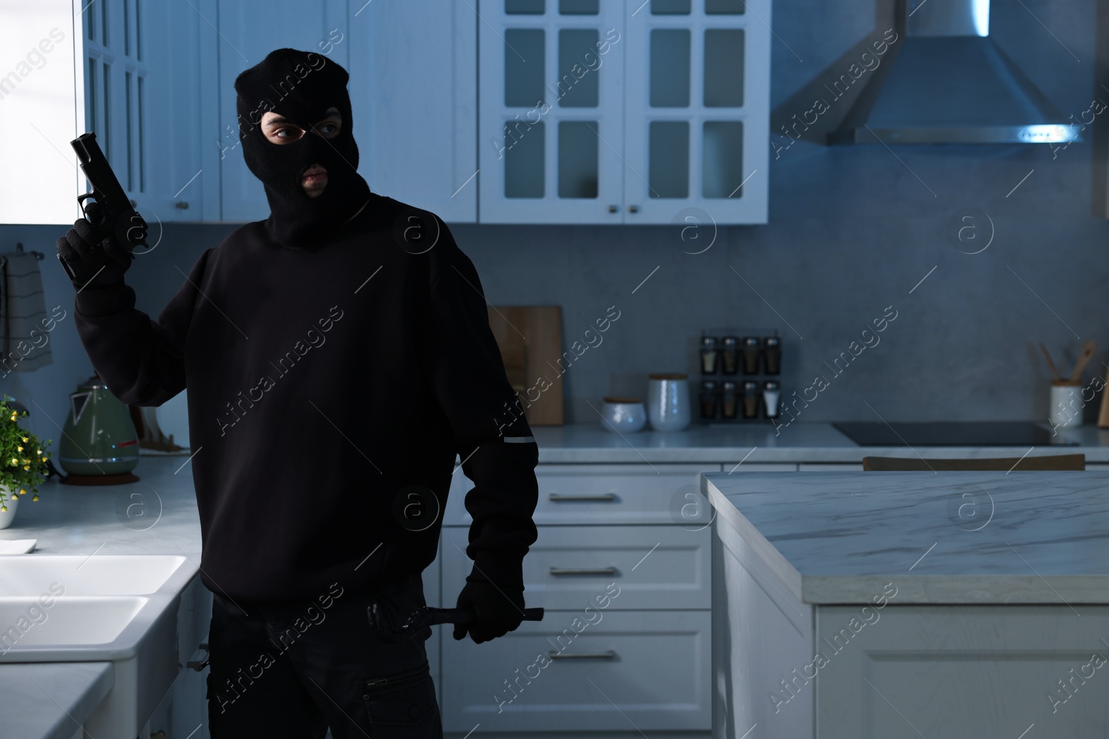 Photo of Thief wearing balaclava with gun and crowbar in foreign house. Burglary