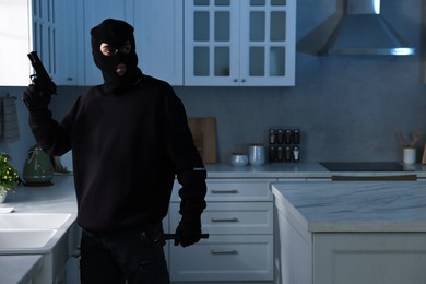 Thief wearing balaclava with gun and crowbar in foreign house. Burglary