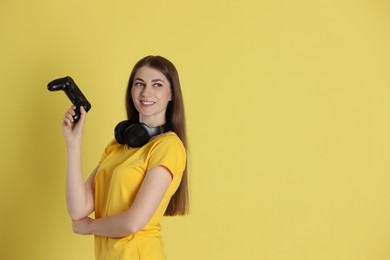 Happy woman with controller on yellow background, space for text