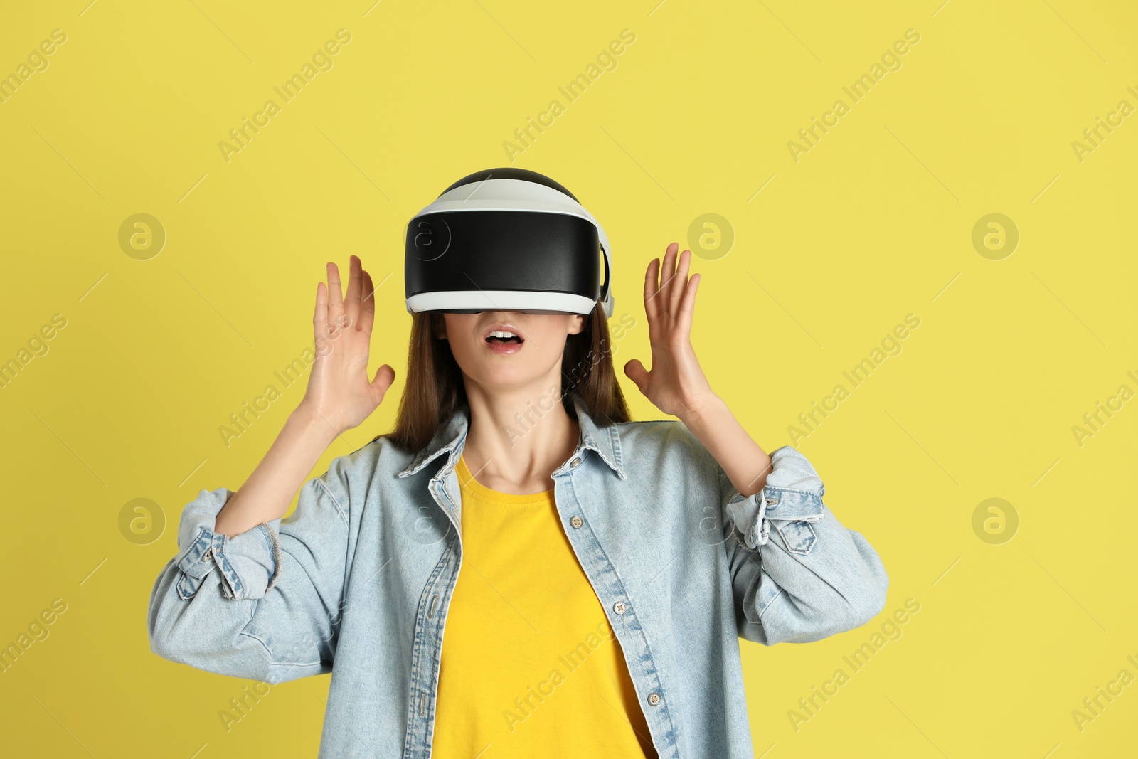 Photo of Surprised woman using virtual reality headset on yellow background