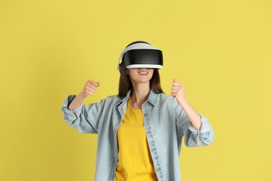 Photo of Smiling woman using virtual reality headset on yellow background