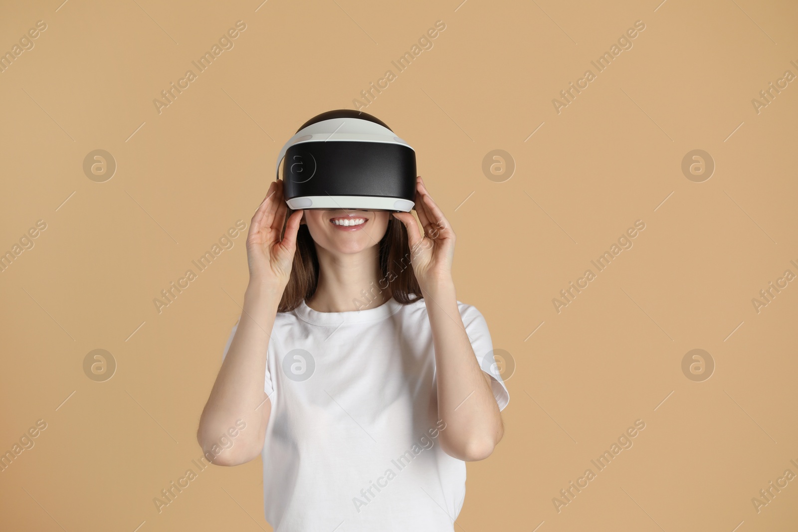 Photo of Smiling woman using virtual reality headset on beige background