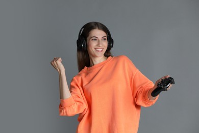 Happy woman in headphones with controller on gray background