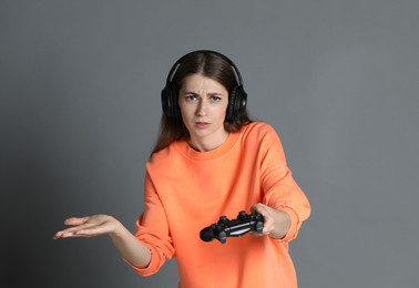 Woman in headphones with controller on gray background, space for text