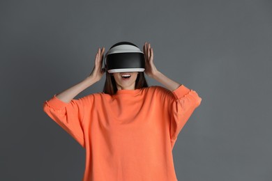 Surprised woman using virtual reality headset on gray background