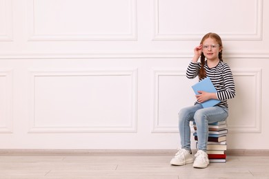 Smiling girl sitting on stack of books indoors. Space for text