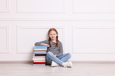 Cute girl sitting with stack of books indoors