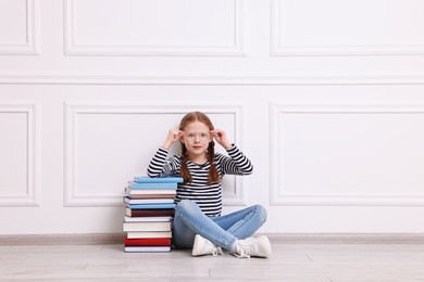 Cute girl sitting with stack of books indoors