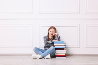 Cute girl sitting with stack of books indoors