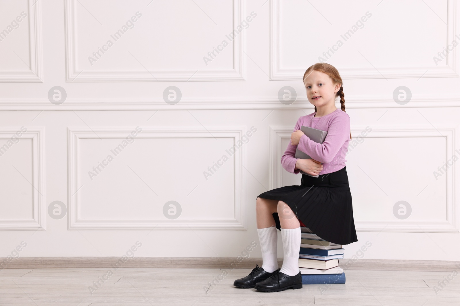 Photo of Smiling girl sitting on stack of books indoors. Space for text