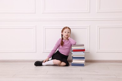 Photo of Little girl with stack of books on floor indoors